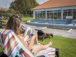 De CocksdorpにあるCozy Chalet Near North Seaのプールの横の芝生の椅子に座って本を読んでいる女性 +19枚の写真