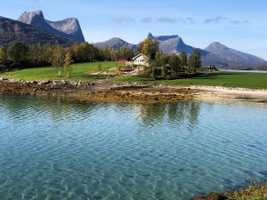 a lake with a house and mountains in the background at Efjord and Stetind Resort - Cabin Kobbernestinden in Ballangen