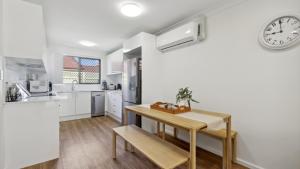 a kitchen with a table and a clock on the wall at Sunset Palms - Stylish Retreat, BBQ, Walk to Beach in Coffs Harbour