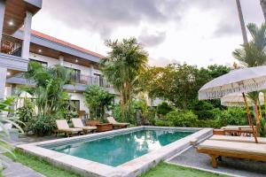 a pool in front of a building with chairs and an umbrella at Lemon Guest House in Canggu