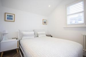 ein weißes Bett in einem weißen Schlafzimmer mit einem Fenster in der Unterkunft Coachman's Cottage- Worthing Beach sleeps 9 in Worthing + 23 Fotos
