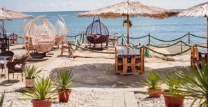 a beach with tables chairs and umbrellas and the ocean at Century Helang Hotel in Pantai Cenang