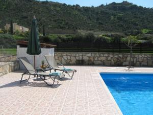 duas cadeiras e um guarda-sol junto a uma piscina em Pangeras Apartments em Pissouri