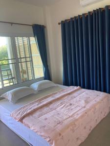 a bedroom with a bed with blue curtains and a window at Huan Janto Homestay - Karuna in Ban Sam Lang