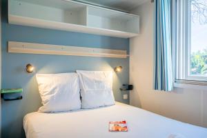 a bedroom with a bed with white pillows and a window at Camping Paradis 4 étoiles A La Corniche La Rochelle Angoulins in Angoulins-sur-Mer