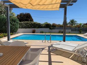 una piscina con sillas, una mesa y una sombrilla en Villa Thea, en Afantou