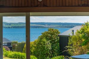 a view of the water from a house window at Lakeview Cottage - Rainbow Point Holiday Home in Taupo