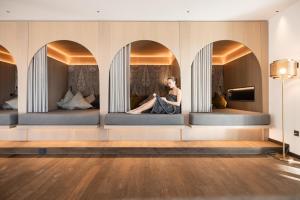 a woman sitting on a bed in a room with three mirrors at Lake Spa Hotel SEELEITEN in Caldaro