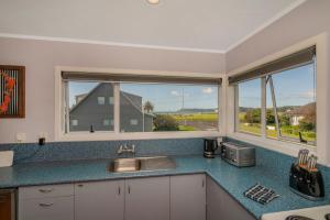 a kitchen with a sink and two windows at Across the Road to the Beach - Beach House in Whitianga