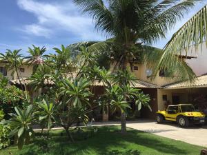 a yellow car parked in front of a building with palm trees at Pousada Villa Joia in Barra de São Miguel