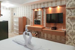 a room with a tv and a swan on a bed at Minimalist and Comfort Studio Podomoro City Deli Medan Apartment By Travelio in Medan