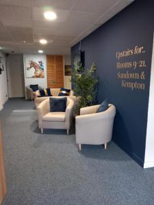 a waiting room with couches and chairs and a wall at Sandown Park Lodge in Esher