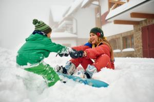 zwei Personen spielen im Schnee auf einem Snowboard in der Unterkunft Pohorje Village Wellbeing Resort - Forest Hotel Videc in Hočko Pohorje