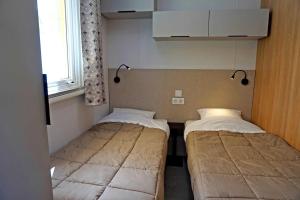 Dos camas en una habitación pequeña con ventana. en Camping 4 étoiles - Parc aquatique - eeiaei, en Givrand