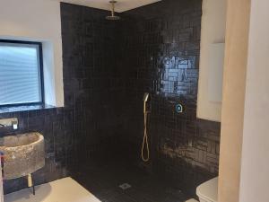 bagno con doccia e parete di piastrelle nere di The Old Milking Barn Loft a Tiverton
