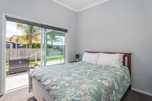 a bedroom with a bed and a sliding glass door at Hosts on the Coast Belair Bach in Whitianga
