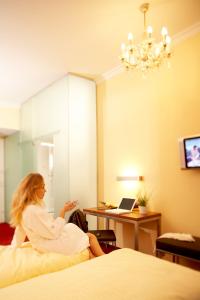 une femme assise sur un lit dans une chambre d'hôtel dans l'établissement Villa Ceconi by Das Grüne Hotel zur Post - 100% BIO, à Salzbourg