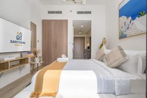 a bedroom with a large white bed and a tv at Santorini Studio Pool View in Dubai