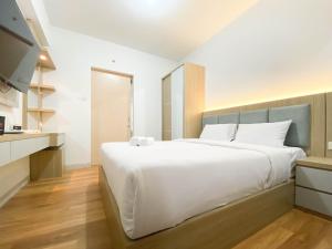 a bedroom with a large white bed and a kitchen at Comfort and Cozy Stay 1BR at The Alton Apartment By Travelio in Semarang
