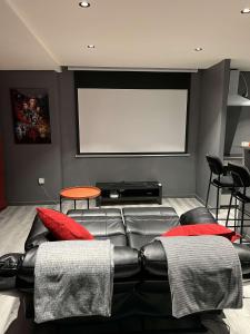 a living room with a black leather couch and a white screen at Suite CinéRoom à 25 min de Paris in Franconville