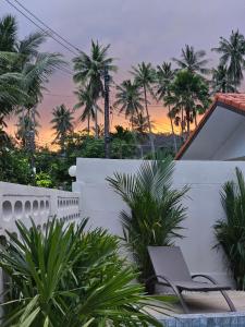 eine Terrasse mit einem Stuhl und Palmen bei Sonnenuntergang in der Unterkunft Nai Harn beach Villa 2 bdr in Rawai Beach