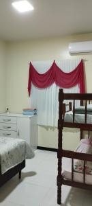 ein Schlafzimmer mit einem Bett und einem Fenster mit einem roten Vorhang in der Unterkunft Apartamento em Penha in Penha