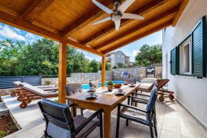 a patio with a wooden table and chairs and a ceiling fan at MY DALMATIA - Sea view villa Nana with private swimming pool in Lukoran