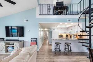 a living room with a couch and a kitchen and a staircase at Dog Friendly 2 Bed Condo! Walk To Beach or Lagoon! in Gulf Shores