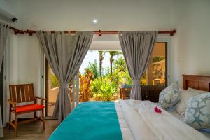 a bedroom with a bed and a chair and a window at Au Cap Self Catering in Anse aux Pins