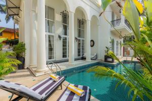 an outdoor swimming pool with two chaise lounges next to a house at ELIVAAS 4 BHK Villa with Pvt Pool & Jacuzzi-Yashgeet in Siolim