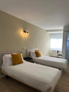 two beds with yellow pillows in a room at Hostal Fronton in Alcobendas