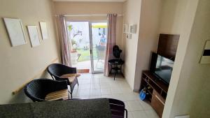 a living room with chairs and a television and a patio at Chalet no paraíso in Maracajaú