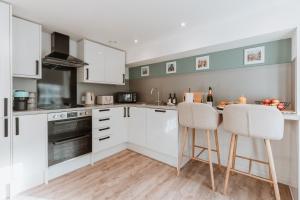 a kitchen with white cabinets and a counter with two stools at 2 Bed Apartment Overlooking the Square Step Out to Shops & Dining in Shrewsbury