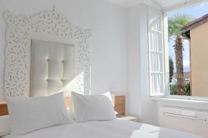 a white bed with white pillows and a window at Caffè dell'Arte Boutique Rooms Locarno in Locarno