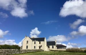 a white house with a blue sky and clouds at Stromabank Hotel, Longhope, Island of Hoy in Stromness