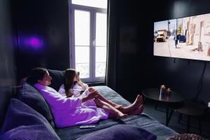 a man and a woman sitting on a couch watching tv at Dreamy Room - Evasion, balnéo & cinéma privé in Angers