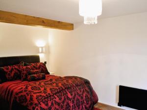 a bedroom with a bed with a red comforter and a television at Dove Cottage in Ampney Crucis