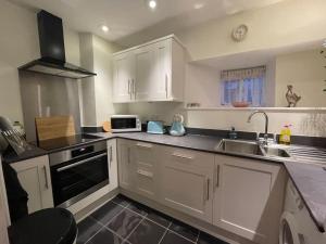 eine Küche mit weißen Schränken und einer Spüle und einer Mikrowelle in der Unterkunft Braunton Breaks - North Beach Cottage in Braunton