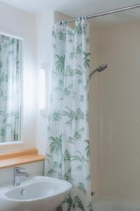 a bathroom with a sink and a shower curtain with palm trees at Kyriad Cannes - Mandelieu in Cannes