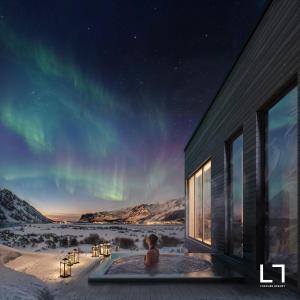 una persona seduta in una vasca idromassaggio sotto l'aurora boreale di Lofoten Arctic Lodge - sea view, jacuzzi & sauna a Lyngværet