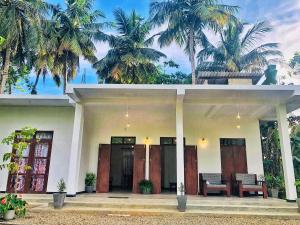 a white house with palm trees in the background at Renu's House By Villa Greenery in Talpe