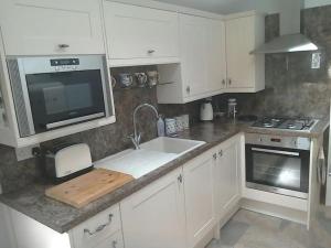 eine Küche mit weißen Schränken und einer Spüle und einer Mikrowelle in der Unterkunft Quarry Cottage in Consett