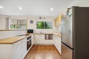 une cuisine avec des armoires blanches et un réfrigérateur en acier inoxydable dans l'établissement Beach Cottage, à Woolgoolga