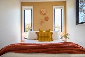 a bed with a yellow pillow and two windows at Gumleaf in Coles Bay