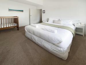 a bedroom with a large white bed and a crib at Family Getaway Opposite Warilla Beach in Lake Illawarra +19 photos