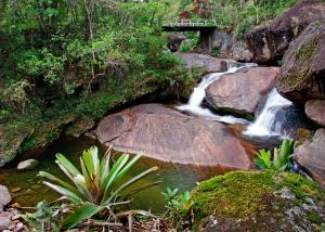 a creek with a bridge and a waterfall at Pousada da Gruta in Visconde De Maua