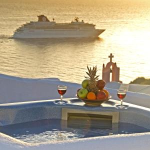 a bowl of fruit with two glasses of wine and a cruise ship at Marizan Caves & Villas in Oia