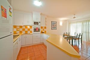 a kitchen with white cabinets and a table in it at at Beach Court Holiday Villas in Airlie Beach