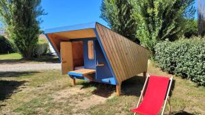 a tiny house sitting on the grass next to a red chair at Camping Kerlaudy La pause Atypi'k in Plouénan