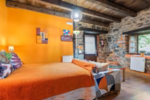 a bedroom with an orange bed and a stone wall at Loureiro in Vega de Logares